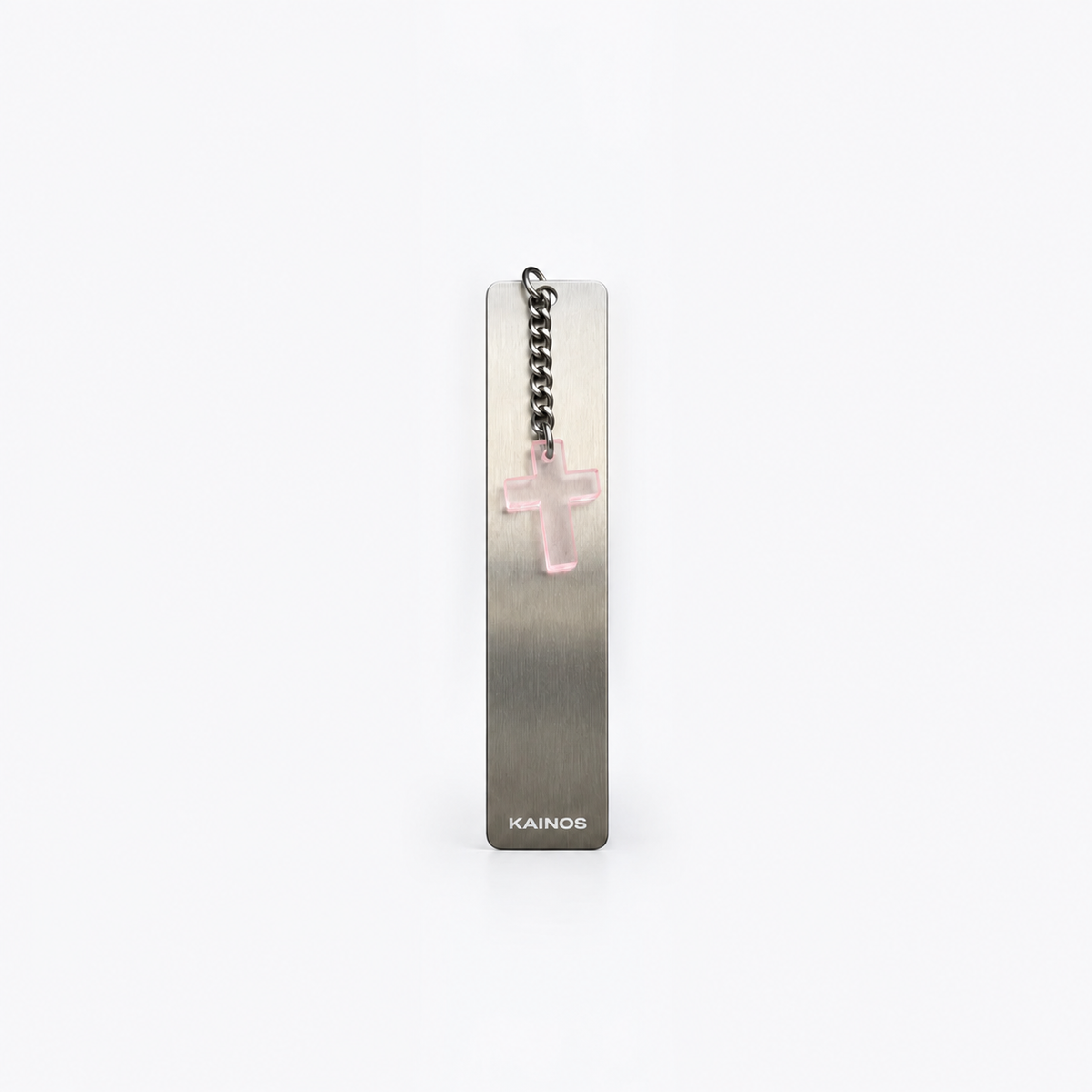 A slim rectangular metal bookmark with a brushed silver finish, featuring a small pink translucent cross charm on a black chain and the brand name 'KAINOS' at the bottom, set against a plain white background.