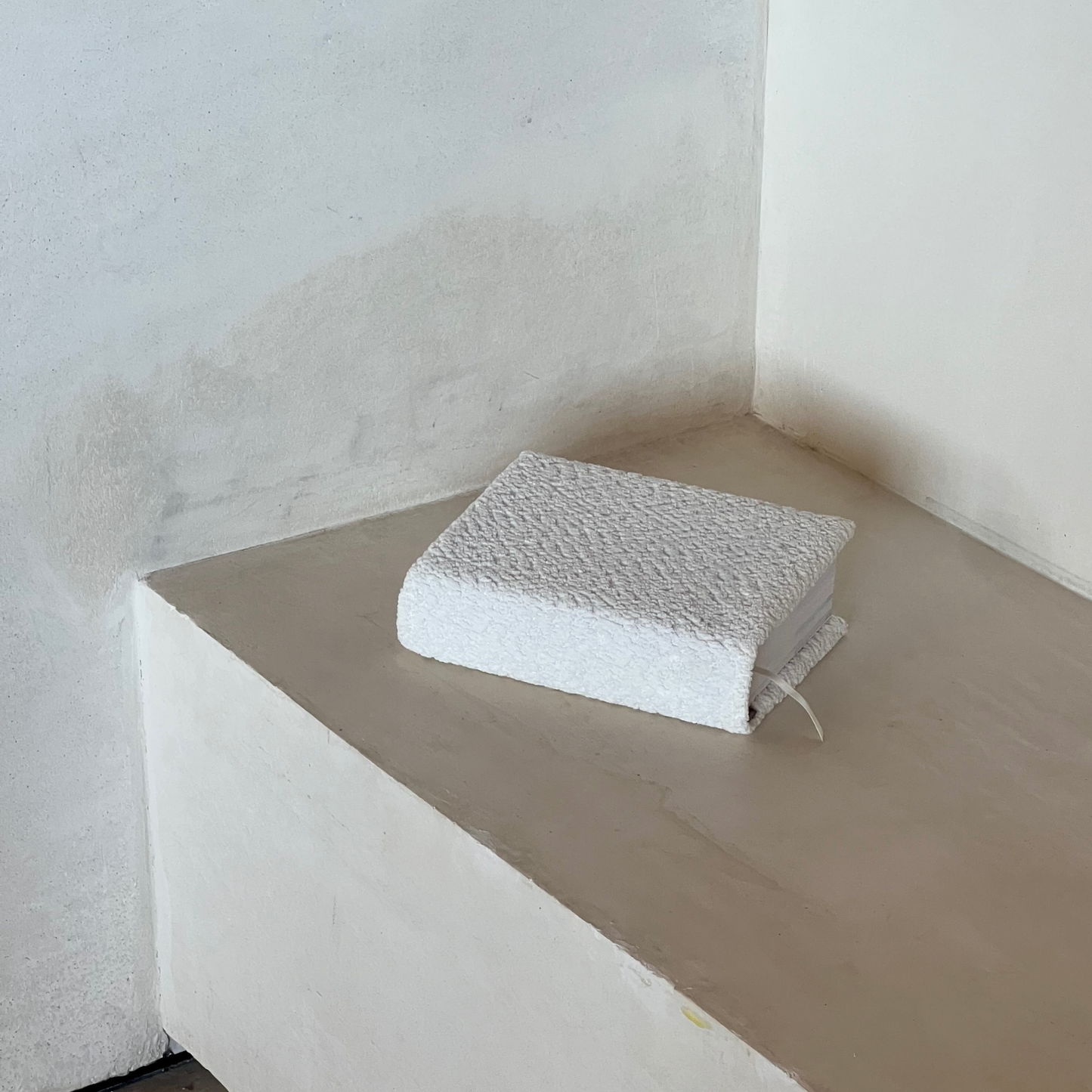 White textured Kainos Bare Boucle Bible cover on a concrete ledge with a white wall background