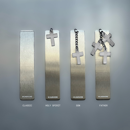 Four rectangular metallic bookmarks or tags with hanging cross charms are arranged on a smooth gray surface. From left to right, the designs are labeled Classic, Holy Spirit, Son, and Father, with the word 'KAINOS' visible near the bottom of each piece.