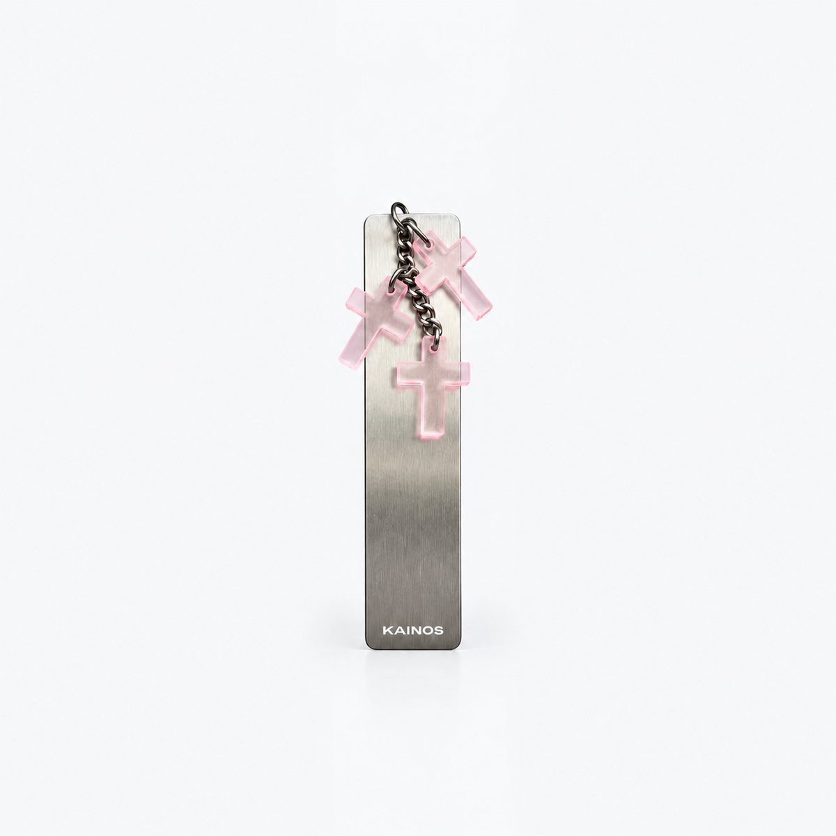 A slim rectangular metallic bookmark or card holder with a brushed silver finish, featuring a small hanging chain with three translucent pink cross charms and the brand name KAINOS printed near the bottom.