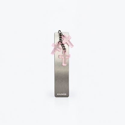 A slim rectangular metallic bookmark or card holder with a brushed silver finish, featuring a small hanging chain with three translucent pink cross charms and the brand name KAINOS printed near the bottom.