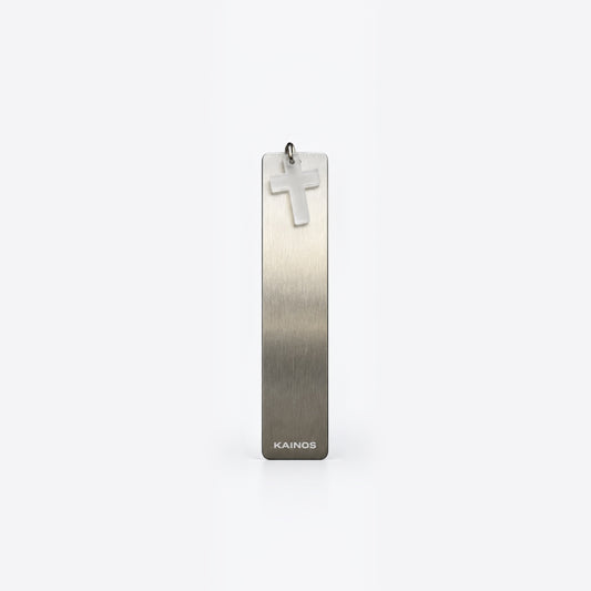A vertical rectangular brushed metal pendant with a small cross charm at the top and the brand name KAINOS near the bottom, shown on a clean light gray background.