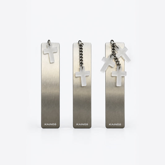 Three Kainos rectangular metal pendant earrings with brushed silver gradients, each featuring a small white cross charm and hanging chain, displayed on a clean white background.